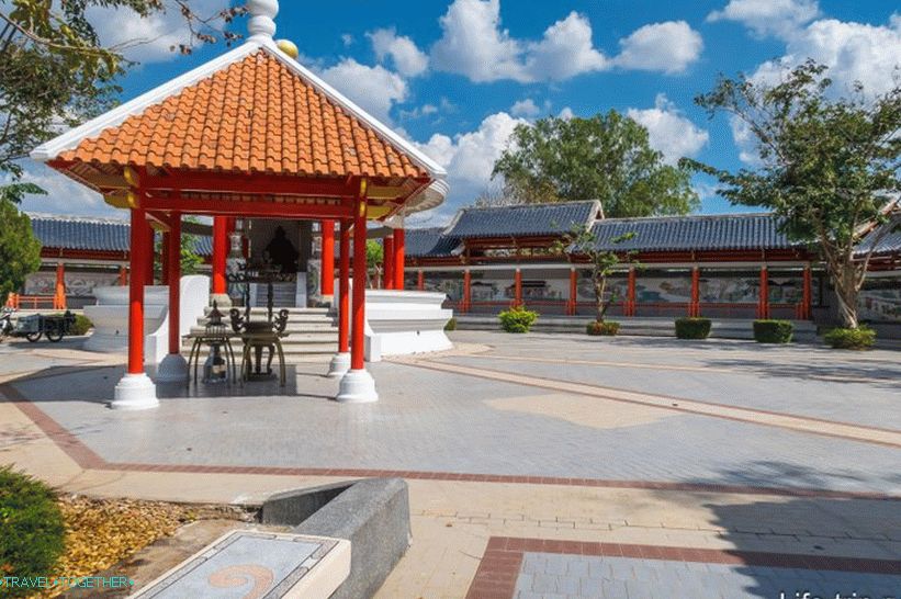 Skulptura kineskog božanstva pod krovom i zidom uz park, sa slikama na pločici